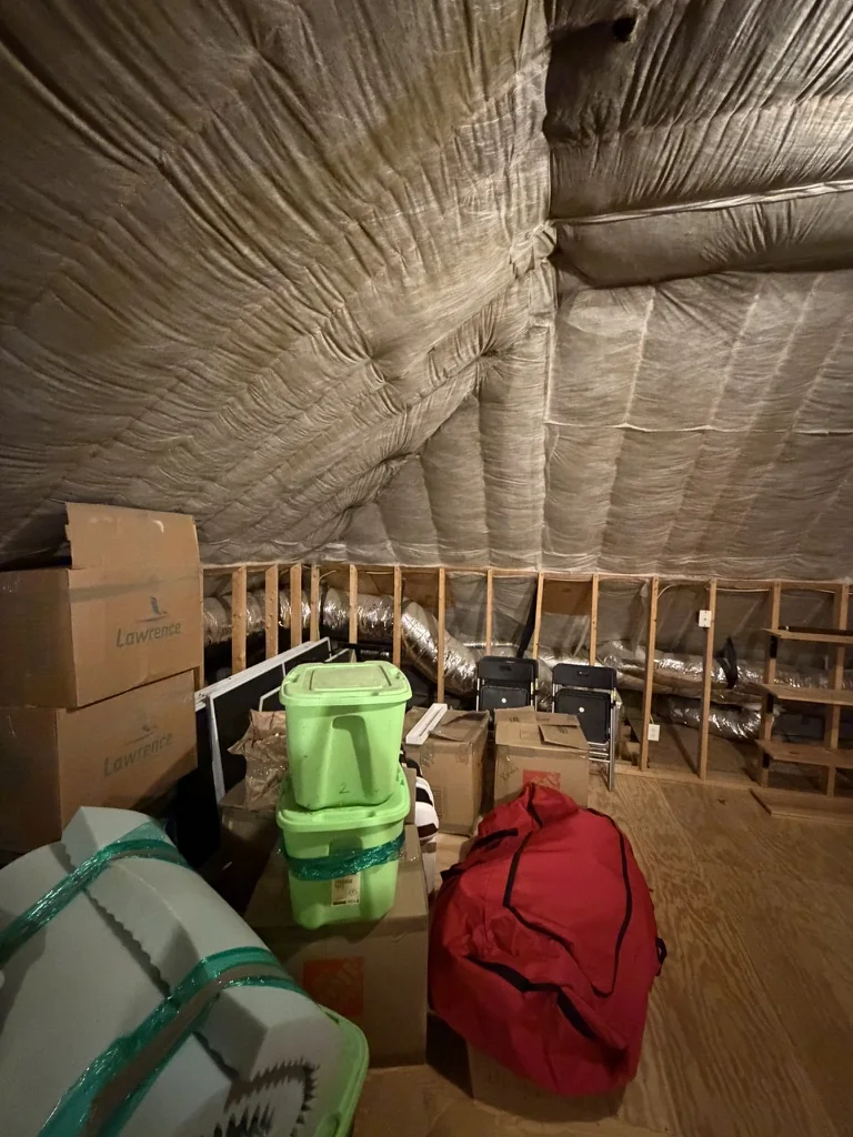 Unfinished attic before conversion with exposed insulation, framing, and stored household items