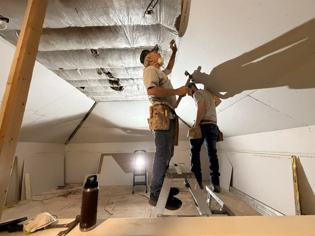Crew installing drywall along the sloped attic ceiling during gym construction