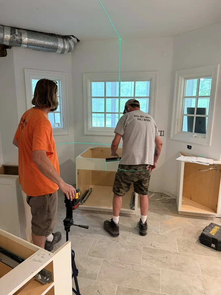 Installers positioning new kitchen cabinets around the bay window using a laser level
