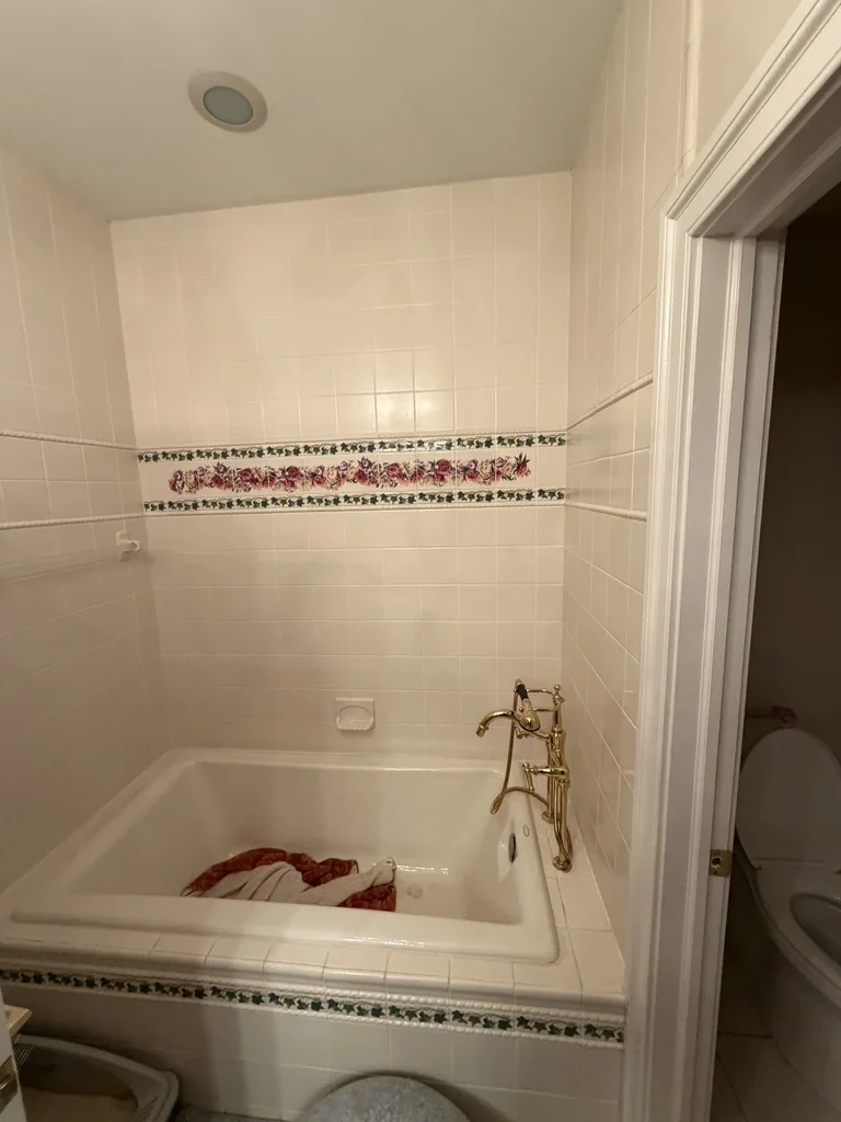 Original built-in guest bathroom tub with floral tile border before conversion to a walk-in shower