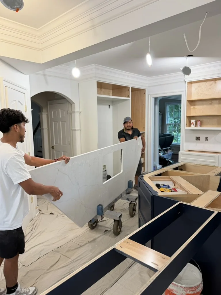 Countertop installers moving a veined quartz slab beside the blue kitchen island