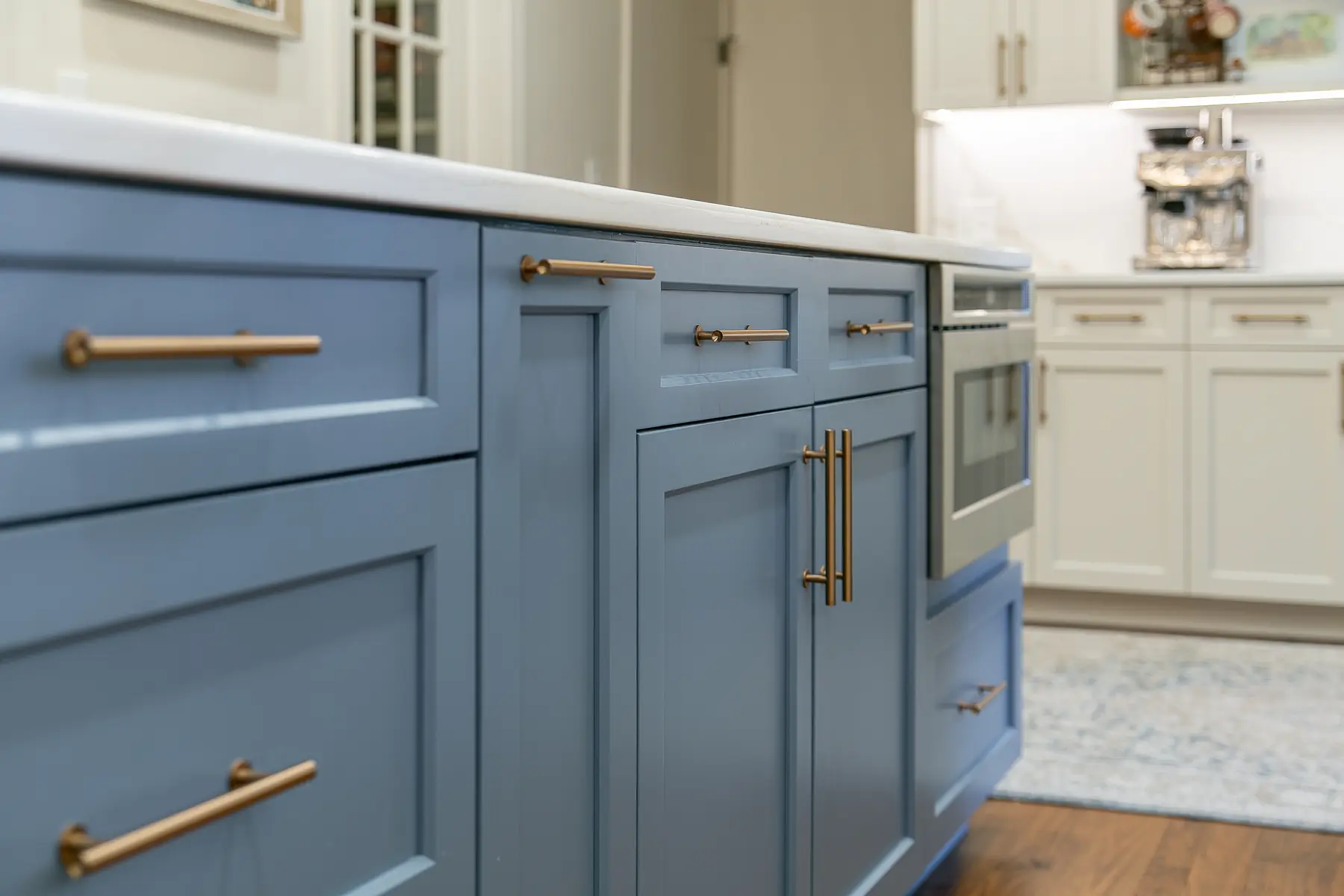 Close view of deep blue shaker island cabinetry with long brass pulls and a white stone countertop