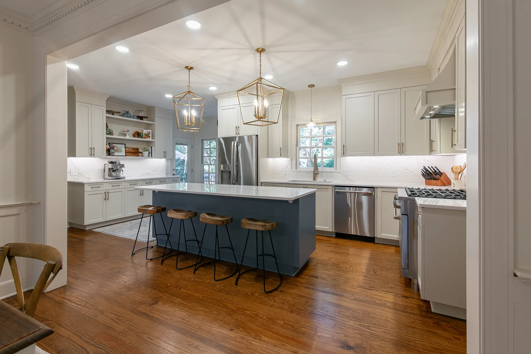 Wide view of a completed Kingsmill kitchen remodel with a deep blue seating island, warm white cabinetry, brass lantern pendants, and marble-look slab surfaces by VanFleet Homes