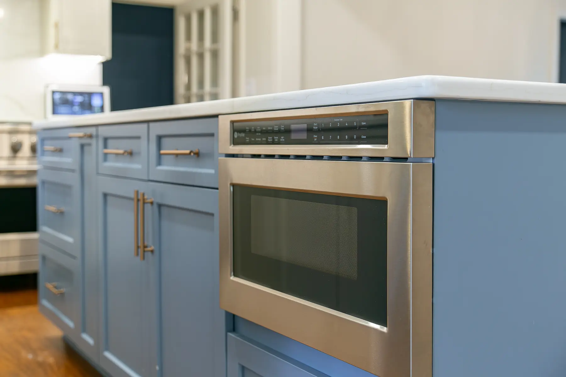 Built-in microwave integrated into blue island cabinetry with brass hardware and finished end panels