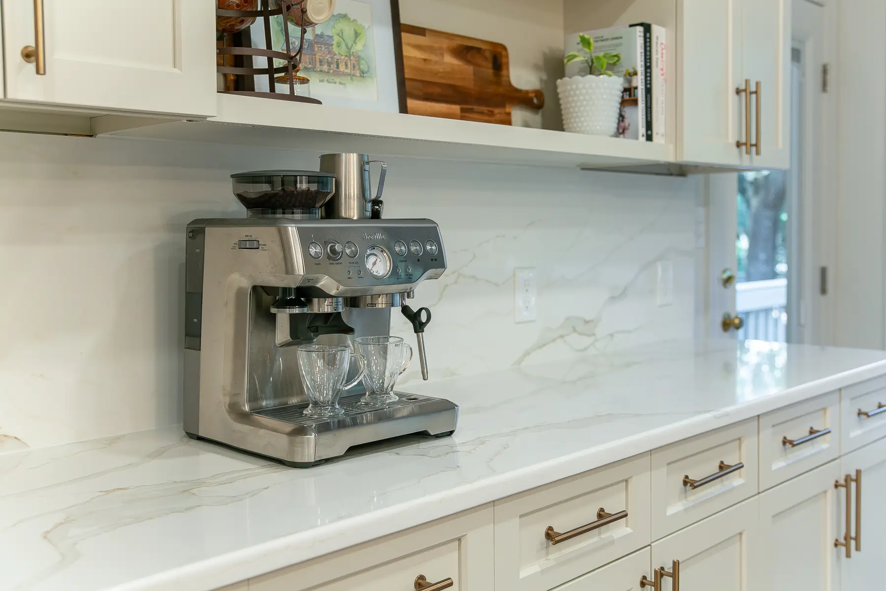 Kingsmill coffee station with open shelving, warm white cabinetry, undercabinet lighting, and full-height slab backsplash