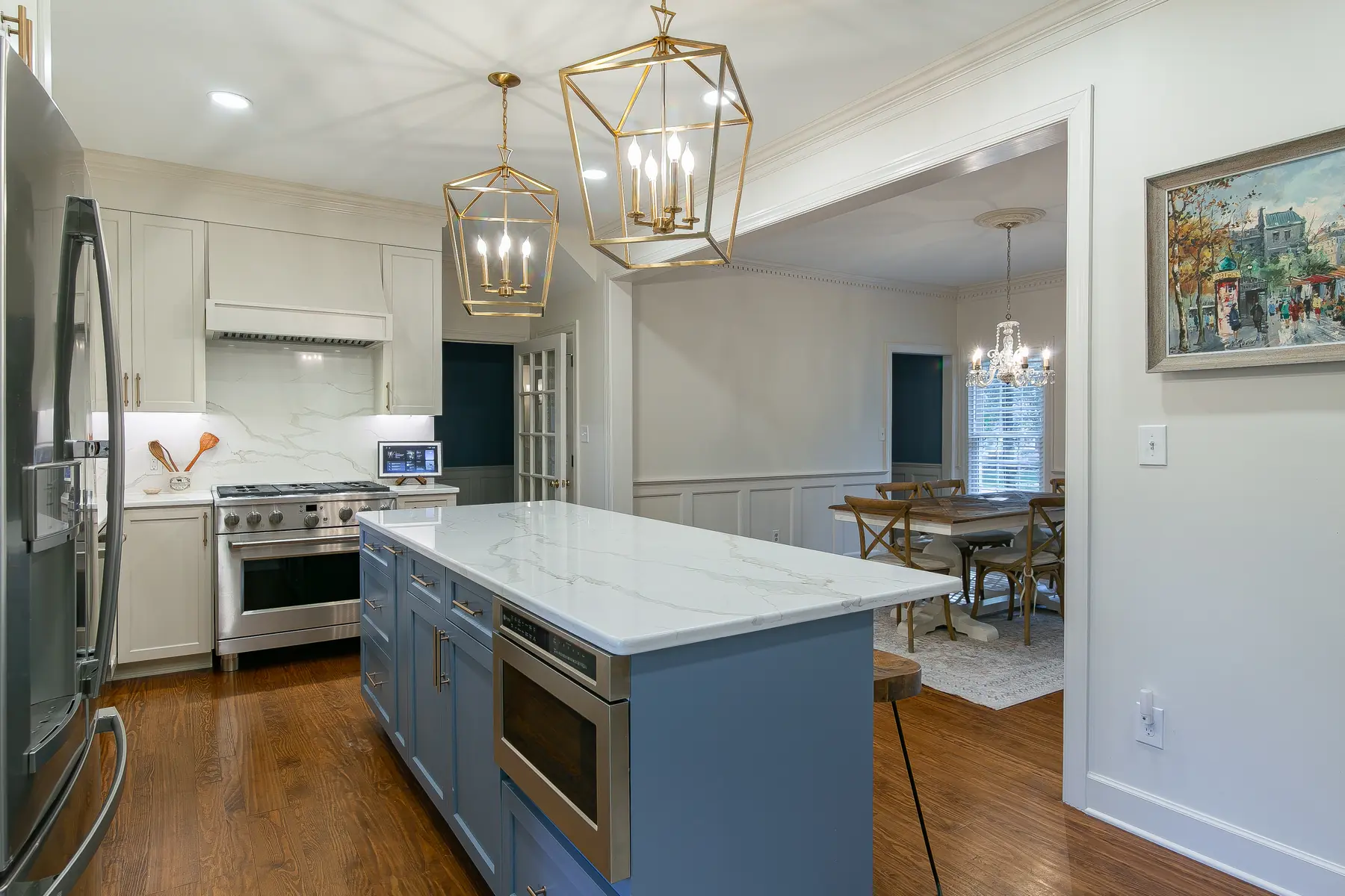 Blue kitchen island with built-in microwave, quartz-style countertop, brass lighting, and open connection to the dining room