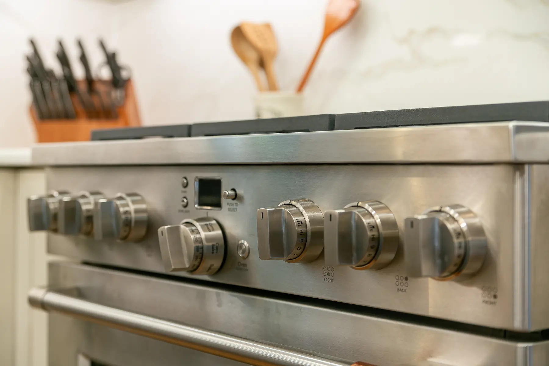 Professional stainless range controls framed by marble-look backsplash and warm kitchen accents