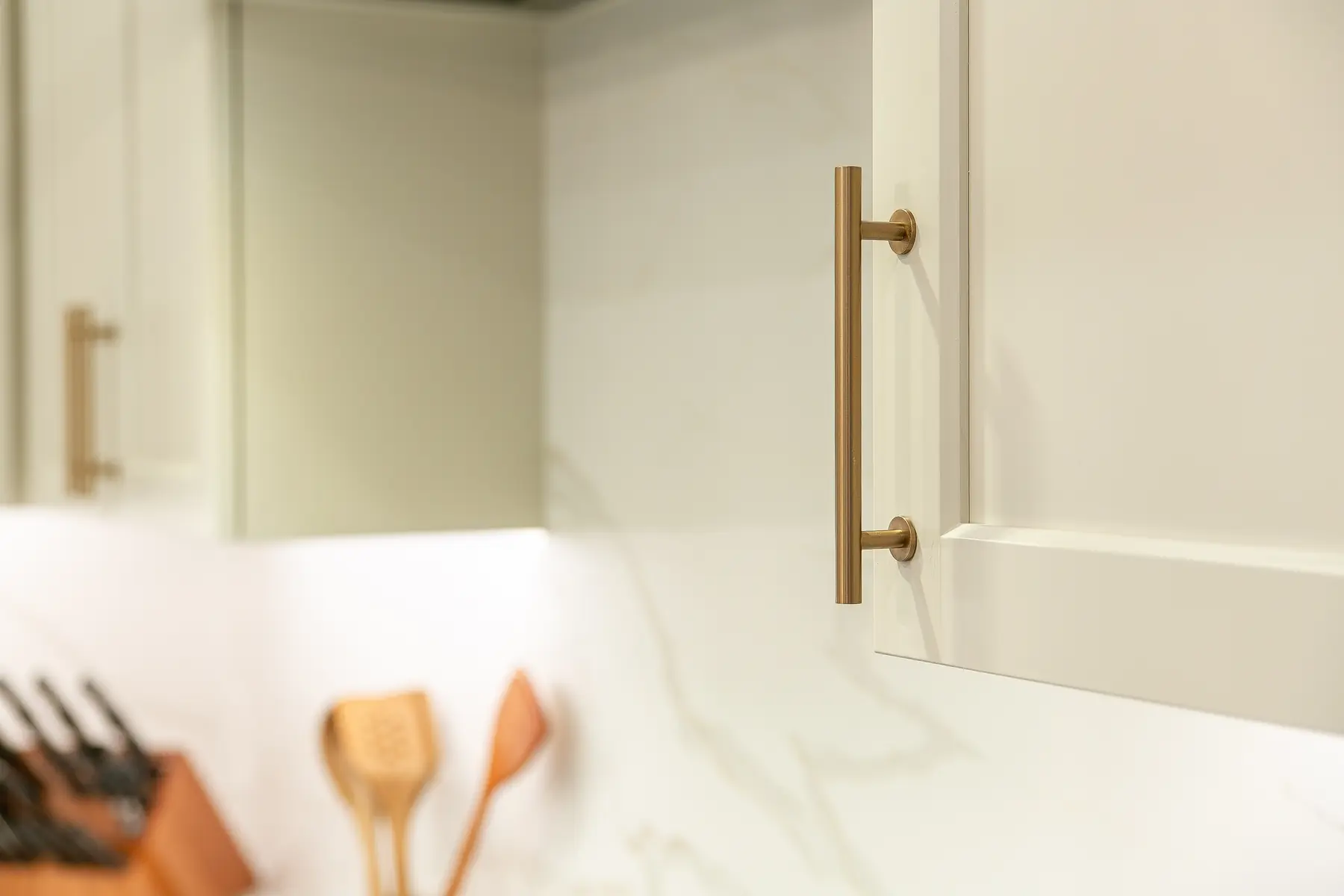 Shaker cabinet door and slim brass pull detail against the softly veined kitchen backsplash